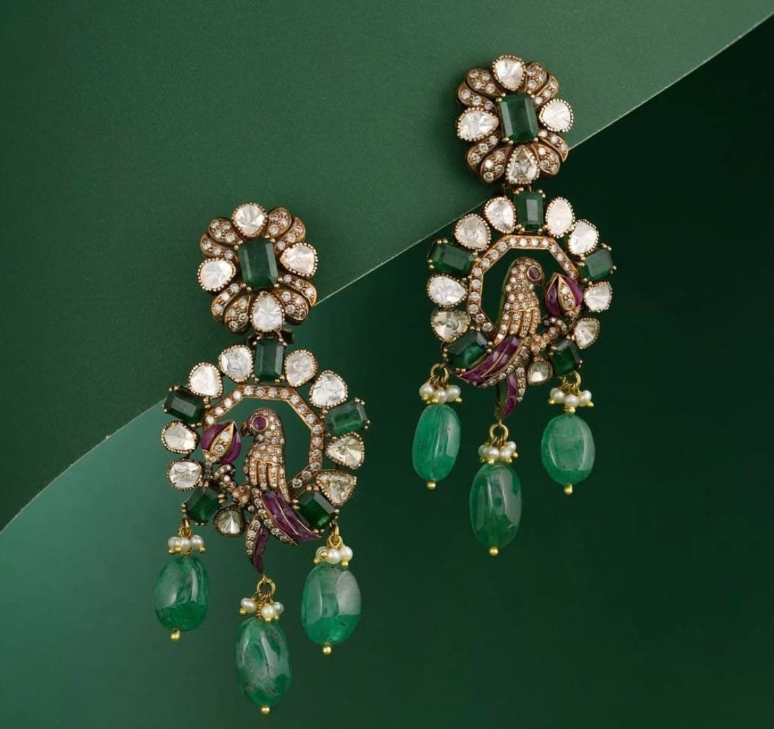 Emerald Aviary — A bird perched inside a ring of uncut stones, three emerald drops swinging beneath on pearl-capped wires.